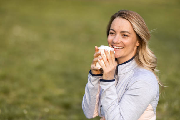 smiling woman holding disposable coffee cup in nature